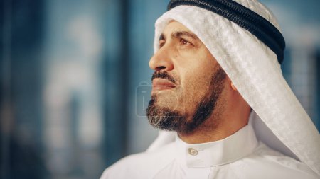 Téléchargez les photos : Portrait d'un homme d'affaires musulman prospère en tenue traditionnelle Souriant doucement, portant du kandura blanc et de l'agal noir Garder un ghutra en place. Arabie saoudite - en image libre de droit