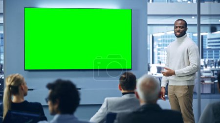 Foto de Evento de presentación de productos modernos: El hombre de negocios negro habla, explica el concepto, utiliza la pantalla principal de croma verde TV. Conferencia de prensa del Grupo de Diversos - Imagen libre de derechos