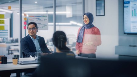 Photo for Multi-Ethnic Office Conference Room. Brilliant Muslim Female CEO Wearing Hijab does Presentation for Group of Managers Talking, Using TV Infographics - Royalty Free Image