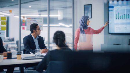 Photo for Multi-Ethnic Office Conference Room. Brilliant Muslim Female CEO Wearing Hijab does Presentation for Group of Managers Talking, Using TV Infographics - Royalty Free Image
