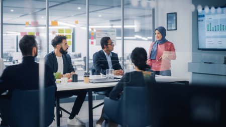 Photo for Multi-Ethnic Office Conference Room. Muslim Female CEO Wearing Hijab does Presentation for Group of Managers Talk, Use TV Infographics, Statistics - Royalty Free Image