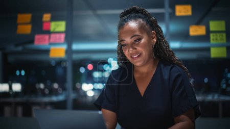 Téléchargez les photos : Portrait d'une femme d'affaires afro-américaine travaillant sur un ordinateur portable à Big City Office tard dans la soirée. Directrice exécutive féminine - en image libre de droit
