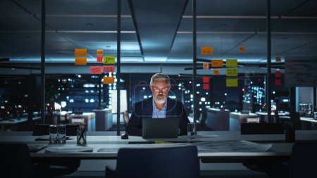 Photo for Successful Senior Businessman Working on Laptop Computer in Big City Office Late in the Evening. Investment Analyst Checking Financial Graphs from - Royalty Free Image
