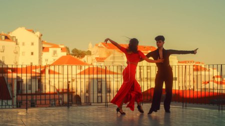 Foto de Hermosa pareja bailando una danza latina fuera de la ciudad con el casco antiguo en el fondo. Sensual danza de dos bailarines profesionales en una puesta de sol en - Imagen libre de derechos
