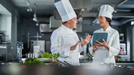 Photo for Restaurant Kitchen: Team of Asian and Black Female Chefs use Tablet Computer while Cooking Delicious and Authentic Food. Perfect Teamwork in Preparing - Royalty Free Image