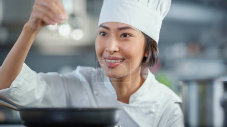 Photo for Restaurant Kitchen: Portrait of Asian Female Chef Fries Uses Pan, Seasons Dish with Herbs and Spices, Smiles. Professional Cooking Delicious and - Royalty Free Image