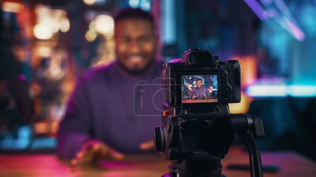 Foto de Guapo joven afroamericano hablando en el micrófono mientras graba programa de radio desde su apartamento Loft. feliz negro macho hablando en cámara y - Imagen libre de derechos