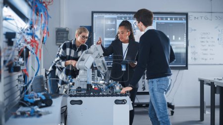 In Robotics Development Laboratory: Black Female Teacher and Two Students Work With Prototype of Robotic Hand (en inglés). Estudiante joven diciendo algo con