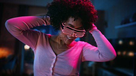 Téléchargez les photos : Fermer Portrait d'une jeune femme latine multiethnique diversifiée dansant dans des lunettes lumineuses au néon futuristes, faisant la fête à la maison dans un appartement Loft - en image libre de droit