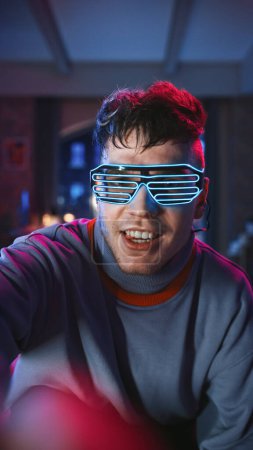 Vertical Screen: Portrait of a Handsome Young Man Dancing in Stylish Futuristic Neon Glowing Glasses, Having a Party at Home in Loft Apartment