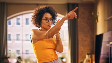 Téléchargez les photos : Portrait de jeune femme noire multiethnique dansant dans des vêtements décontractés confortables, s'amusant à la maison dans l'appartement Loft. Enregistrement de vidéos virales drôles pour - en image libre de droit