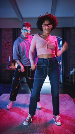 Vertical Screen: Beautiful Stylish Multiethnic Couple in Futuristic Neon Glowing Glasses, Dance and Have a Party at Home in Loft Apartment. Recording