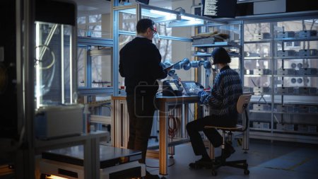 Geschickter männlicher Ingenieur mit Tablet berät junge Computerentwickler, während er Code für das Roboterprogramm für Gliedmaßen schreibt. Menschen konstruieren automatisiert