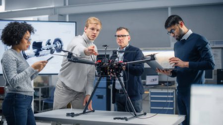 Diverse Luftfahrtingenieure arbeiten gemeinsam an einer neuen ferngesteuerten Drohne, diskutieren aktiv, nutzen Geräte im wissenschaftlichen Labor. Inbetriebnahme und