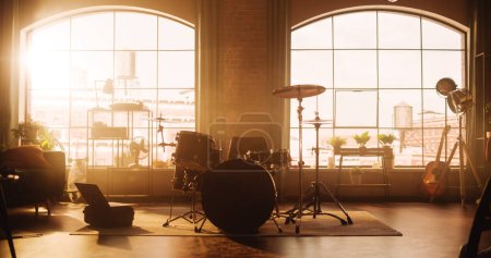 Photo for Establishing Shot: Music Rehearsal Studio in Loft Room with Drum Set in the Middle of It. Stylish Interior with Two Big Windows, Cozy Sofa, Shelves - Royalty Free Image