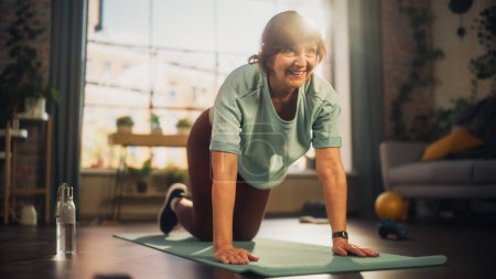 Photo for Strong Fit Senior Woman Training on a Yoga Mat, Doing Stretching and Core Strengthening Exercises During Morning Workout at Home in Sunny Apartment - Royalty Free Image