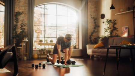 Téléchargez les photos : Fit Athletic Strong Young Man Training and Strengthening Arm Muscles with Dumbbell Exercises During Morning Workout at Home in Sunny Apartment - en image libre de droit
