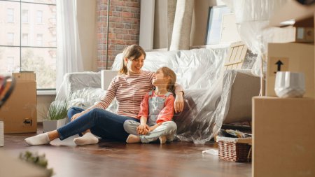Téléchargez les photos : Moving Happy Mother and Daughter Talk, Sitting on a Living Room floor of their New Cozy Home. Cheerful Young Family, Dream, Imagine Good Times, Plan - en image libre de droit
