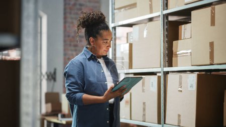 Portrait of a Worker Checking Inventory, Writing in Tablet Computer. Black Woman Working in a Warehouse Storeroom with Rows of Shelves Full of Parcels