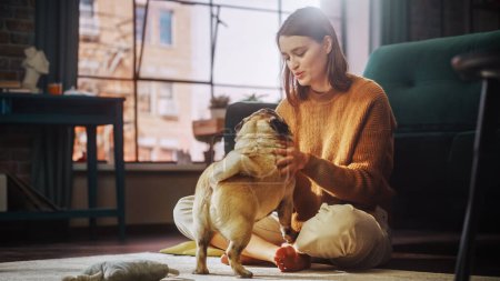 Photo for Beautiful Young Woman Cuddles Her Adorable Little Pug at Home. Girl Plays with Her Dog, Gorgeous Pedegree Best Friend. She Teases, Pets and Scratches - Royalty Free Image
