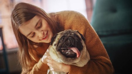 Photo for Beautiful Young Woman Cuddles Her Adorable Little Pug at Home. Girl Plays with Her Dog, Gorgeous Pedegree Best Friend. She Pets and Scratches Super - Royalty Free Image