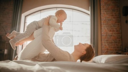 Photo for Young Caring Mother Playing and Nursing Adorable Baby at Home. Beautiful Mom and Cute Little Infant Child Cuddling in Bedroom. Motherhood Tender - Royalty Free Image