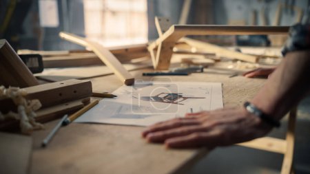 Young Carpenter Reading Blueprints and Starting to Assemble Parts of a Wooden Chair with a Rubber Hammer. Stylish Furniture Designer Working in a