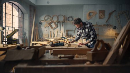 Wide Shot of an Artisan Furniture Designer Reading Blueprint and Starting to Assemble Legs of a Wooden Chair. Stylish Carpenter Working in a Studio in
