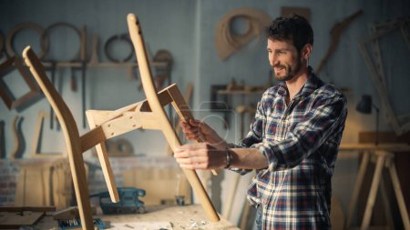 Jeune charpentier élégant assemblant les pièces d'une chaise en bois. Designer professionnel de meubles travaillant dans un studio dans un espace Loft avec des outils sur les murs