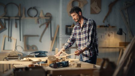 Young Carpenter Reading Blueprints and Starting to Assemble Parts of a Wooden Chair with a Rubber Hammer. Stylish Furniture Designer Working in a
