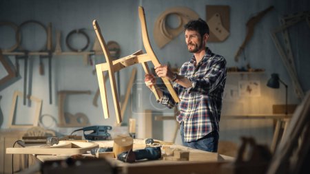 Young Stylish Carpenter Assembling Parts of a Wooden Chair. Professional Furniture Designer Working in a Studio in Loft Space with Tools on the Walls