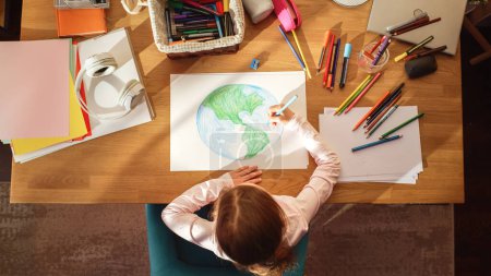 Ansicht von oben: Kleines Mädchen zeichnet unseren schönen Planeten Erde. Sehr talentiertes Kind hat Spaß zu Hause und stellt sich unseren Heimatplaneten als einen glücklichen Ort mit