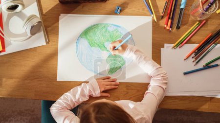Top View: Little Girl Drawing Our Beautiful Planet Earth. Very Talented Child Having Fun at Home, Imagining Our Home Planet as a Happy Place with