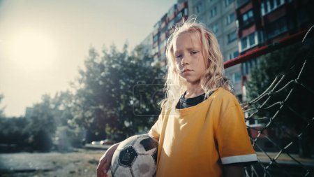 Téléchargez les photos : Talentueuse fille jouant au football avec des garçons de quartier. Jeune footballeur en T-shirt jaune tenant un ballon de football dans le quartier, debout Suivant - en image libre de droit