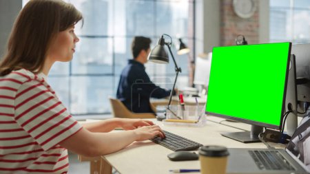 Retrato de una joven blanca usando una computadora con pantalla verde en una espaciosa oficina brillante. Editor femenino usando la llave del croma para la pantalla