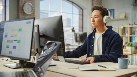 Photo for Portrait of Asian Male Employee Working on Computer in a Modern Office During the Day. Creative Graphic Designer Inspired While Listening to Music on - Royalty Free Image