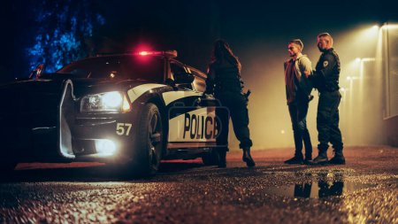 Photo for Two Police Officers Arrest Suspect, Put Him in the Backseat of Patrol Car. Officers of the Law Detain, Handcuff Criminal. Cops Arresting Felon, Fight - Royalty Free Image