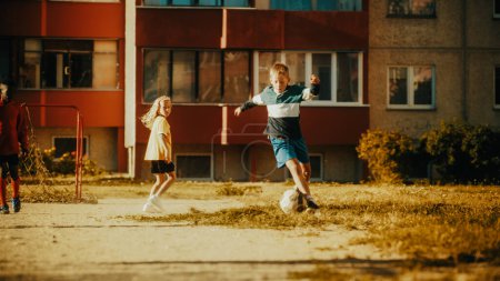Junge talentierte Fußballspieler dribbeln und ein Tor schießen in einem Nachbarschaftsfußballspiel mit verschiedenen multikulturellen Freunden. Junge feiert
