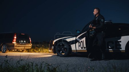 Téléchargez les photos : Portrait of Middle Aged Caucasian Officer Stepping out of a Police Car and Approaching a Pulled Over Vehicle with Caution. Cops Responding to a 911 - en image libre de droit