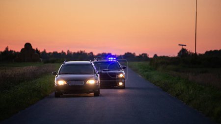 Speeding Driver Gets Pulled Over By Police Patrolling Car . Wide Shot of the Two Cars Stopped in a Road Crossing an Open Field. Drunk Driver Gets