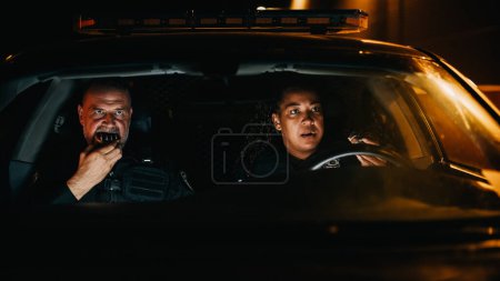 Foto de Punto de vista: Dos oficiales de policía asociados detectan un asalto en la calle oscura mientras comen rosquillas en el coche. Alerta a los oficiales listos para el servicio. Sorprendido. - Imagen libre de derechos