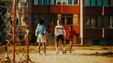 Téléchargez les photos : Heureux amis multiethniques divers jouant au football dans leur cour par une journée ensoleillée en été. Garçons et filles joyeux qui aiment le sport en plein air sur un - en image libre de droit
