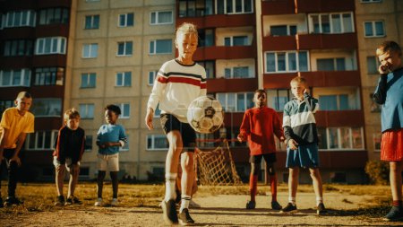 Téléchargez les photos : Portrait d'un jeune garçon jouant à Kick-Ups avec un ballon de football avec des amis dans un quartier. Happy Multicultural Kids in Post soviétique Europe de l'Est - en image libre de droit