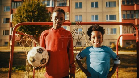 Portrait of Two Young Talented African Boys Standing Together while Looking at Camera and Smiling. Older Brother Holding a Soccer Ball. Black Kids