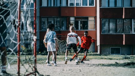 Téléchargez les photos : Amis multiethniques divers jouant au soccer à l'extérieur dans la cour arrière urbaine. Jeune Afro-Américain Garçon Dribbling, Passing opposants Seul avec le ballon et - en image libre de droit