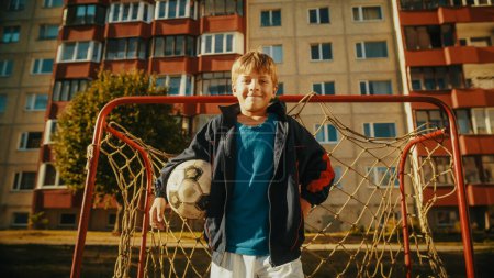 Téléchargez les photos : Portrait d'un garçon heureux portant un manteau de sport tenant un ballon de football dans la cour arrière Jeune joueur de football regardant la caméra, souriant. Debout devant - en image libre de droit