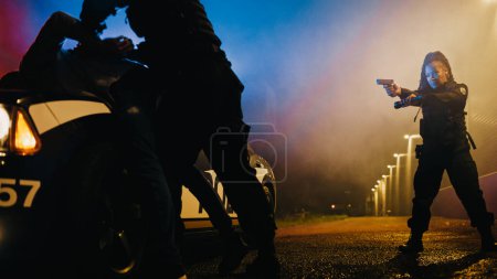 Photo for Male Policeman Forcing a Dangerous Criminal on the Hood of Police Car and Handcuffing him. Camera Focus n Female Holding a Gun and Flashlight and - Royalty Free Image