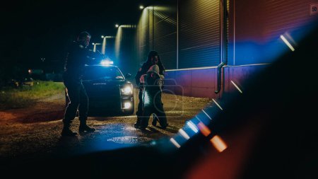 Photo for Two Police Officers Arrest Suspect, Put Him on a Patrol Car Hood. Officers of the Law Handcuff Dangerous Criminal on Dark City Street. Cops Fight - Royalty Free Image