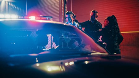 Photo for Two Police Officers Arrest Suspect, Put Him in Patrol Car. Officers of the Law Handcuff Dangerous Criminal on Dark City Street. Officers of the Law - Royalty Free Image