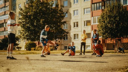 Téléchargez les photos : Jeunes enfants multiethniques jouant avec le ballon dans le quartier. Jeune garçon pratiquant des exercices de soccer, contrôlant le ballon dans les airs. Les amis sont - en image libre de droit
